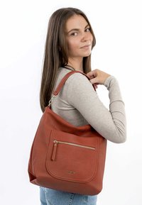 Sac à main en cuir rouge texturé avec une poche zippée à l'avant et une courte sangle, porté par un modèle vêtu d'un haut à manches longues gris clair.