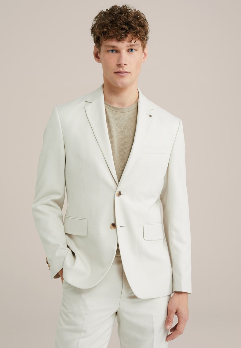 Weißer maßgeschneiderter Blazer mit einem Knopf, zwei Vorderseiten-Taschen und strukturiertem Stoff, kombiniert mit einem hellbeigen Hemd.