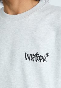 Heled hall, ümar kaelusega sviiter ribitud kaelusega, mille esiosal on must "Wiptopia" logo. Pehme, tekstureeritud kangas.