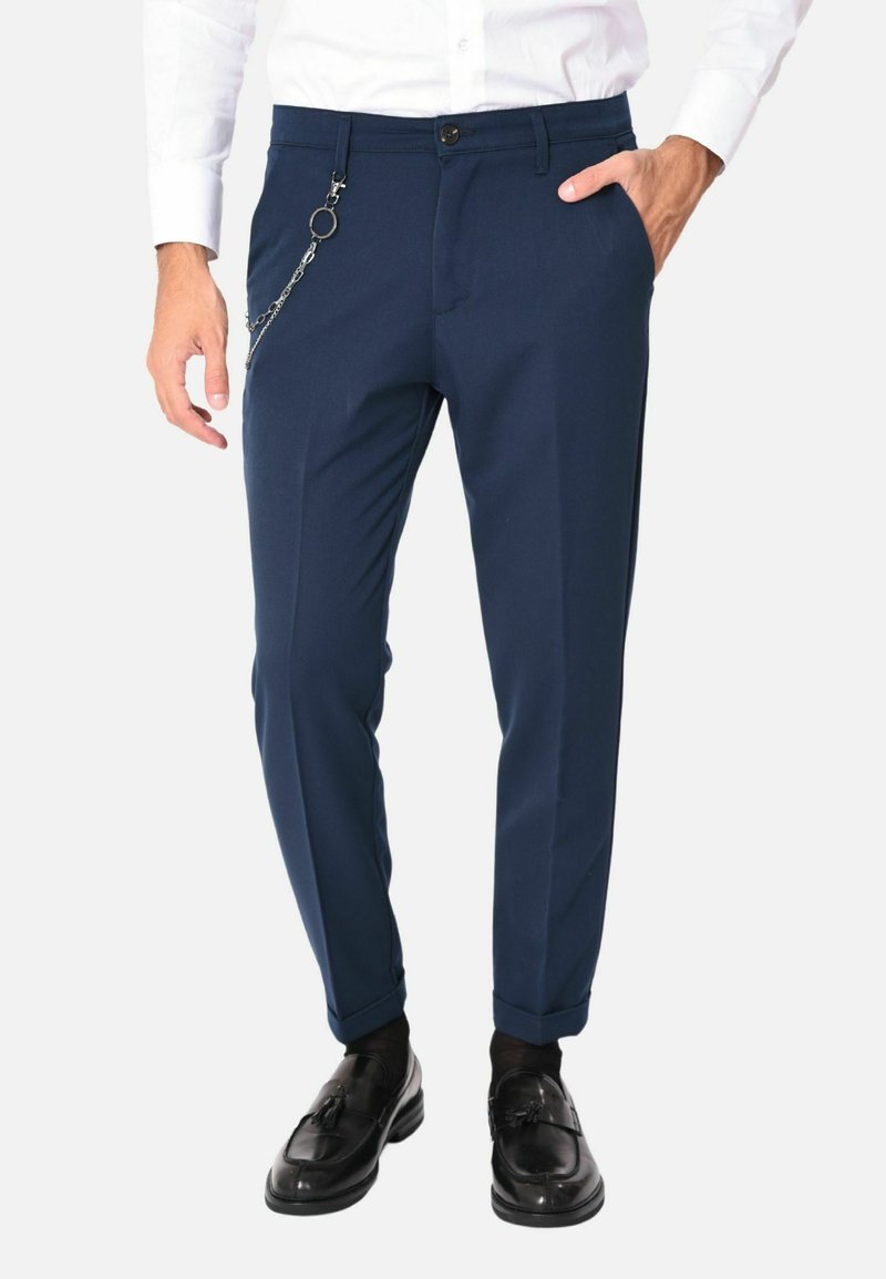 Pantaloni affusolati blu navy, con una vestibilità slim, caratterizzati da un accessorio a catena sul lato, chiusura con zip e bottone, e tasche laterali.