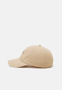 Beige Baumwoll-Baseballmütze mit einem gebogenen Schirm, gesticktem Logodetail auf der Vorderseite und einer strukturierten Krone.