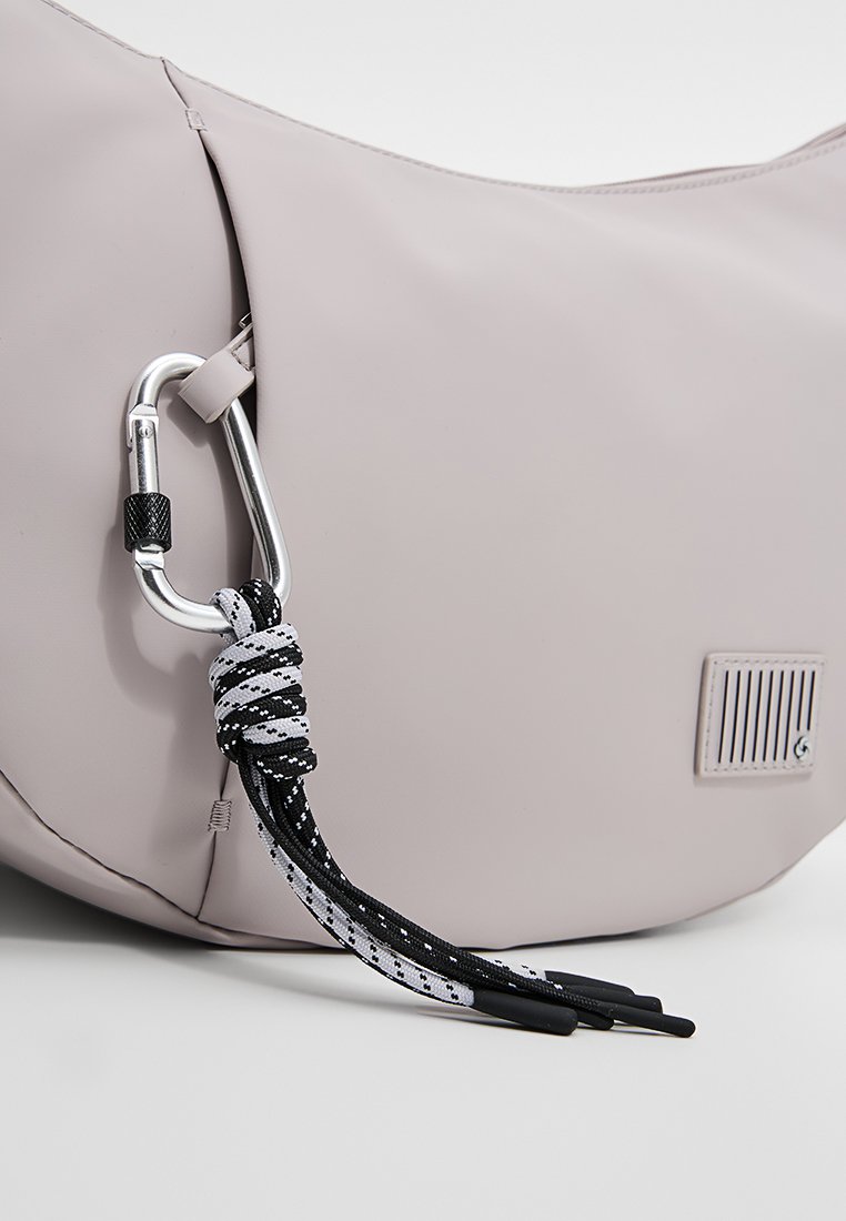 Hellgraue Tasche mit angebrachtem Metallkarabiner, der einen schwarz-weißen geflochtenen Schnur mit Kunststoffspitzen hält, vor einem weißen Hintergrund.