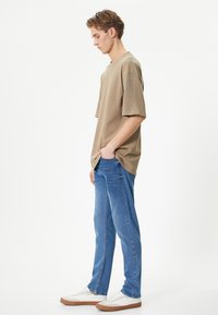 T-shirt beige oversize, maniche corte, scollatura rotonda; abbinato a jeans a gamba dritta blu chiaro e sneakers bianche con suola marrone.