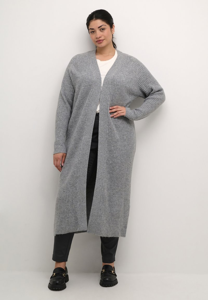 Cardigan lungo grigio a coste con apertura frontale, lavorazione a maglia texturizzata, vestibilità rilassata e maniche lunghe, indossato sopra una maglietta bianca e pantaloni neri.