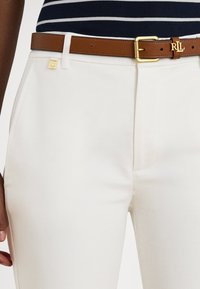 Λευκό εφαρμο�στό παντελόνι με ομαλή υφή, εμπρόσθιες τσέπες και καφέ δερμάτινη ζώνη με χρυσά μεταλλικά στοιχεία και διακριτικό λογότυπο.