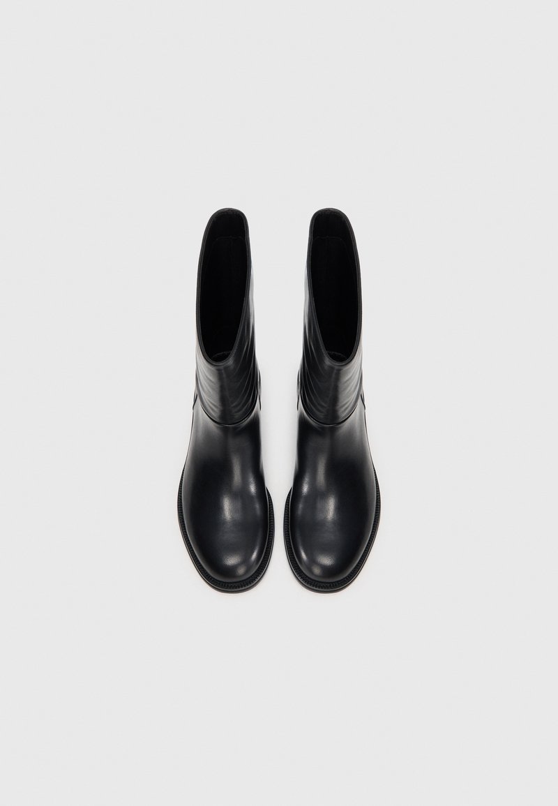 Bottines en cuir noir avec une texture lisse, orteils légèrement arrondis et détails de couture minimaux ; conçues pour un enfilage facile.