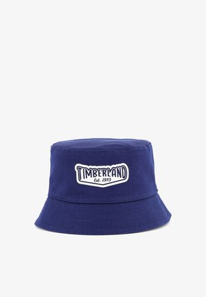 Chapeau seau en coton bleu marine avec un large bord cousu et un patch logo Timberland blanc avec le texte "Est. 1973".
