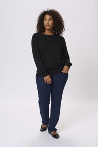 Pull noir avec des manches côtelées, associé à un jean bleu foncé et des chaussures à plat noires. Texture lisse, coupe décontractée et design à col rond.
