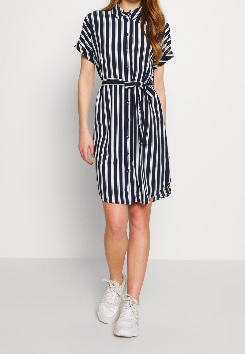 Abito camicia blu navy a righe con maniche corte, chiusura con bottoni e cintura da annodare. Realizzato in tessuto leggero, presenta una vestibilità comoda.