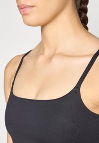 Camiseta de tirantes negros con tiras finas, escote cuadrado y una tela suave y elástica. Vista en primer plano que enfatiza el escote y la zona de los hombros.