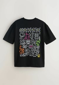 Sort T-shirt med farverige, abstrakte kruseduller inklusive dansende figurer, et tv med et smilende ansigt, en robot samt forskellige dyr og symboler.