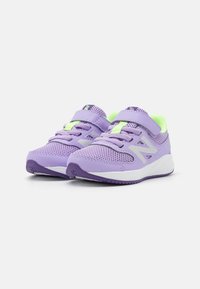 Des chaussures de sport violettes avec une tige en mesh, des accents verts, une sangle sécurisée et des semelles blanches. Elles sont dotées de détails texturés et d'un design moderne.