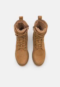 Botas de camurça castanhas com forro de pelúcia sintética, design de atacadores e fecho de zíper lateral. Biqueira arredondada e colarinho acolchoado para conforto.