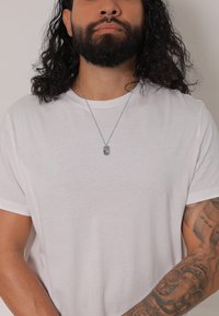 Hvid T-shirt med korte ærmer, rund halsudsk�æring, med en sølv halskæde med et rektangulært vedhæng mod en lys baggrund.