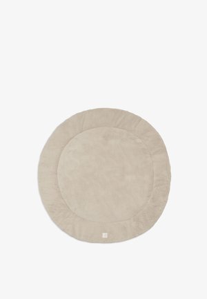 Tapis rond beige en peluche avec une texture douce et une petite étiquette sur un bord sur fond blanc.