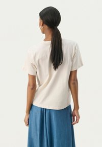 T-shirt beige en coton à manches courtes, col rond et coupe décontractée, associé à une jupe en jean bleue fluide.