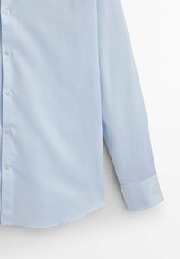 Helles blaues Button-Down-Hemd mit glatter Textur, langen Ärmeln, abgerundetem Saum und weißen Knöpfen. Die Manschette ist ordentlich gefaltet.