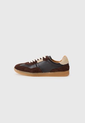 Sneaker mit einer Mischung aus dunkelbraunem Wildleder und glattem schwarzem Leder, mit cremefarbenen Schnürsenkeln und einer hellbraunen Gummisohle. Helle sandfarbene Akzentuierung an der Ferse.
