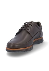 Zapato de cuero marrón con punta redondeada, cordones de cinco ojetes y una suela contrastante en tono beige. Textura suave y detalles de costura mínimos.