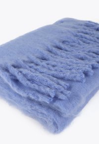 Lyseblå uldtæppe med en blød, fuzzy tekstur og frynser, der skaber et lagdelt, bølgende udseende.