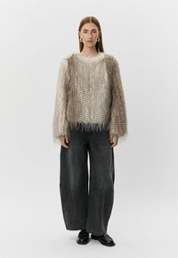 Teksturirani, svijetložuti pulover s resama na rubu, nošen preko širokih crnih traperica. Masivni pleteni dizajn s horizontalnim linijama.