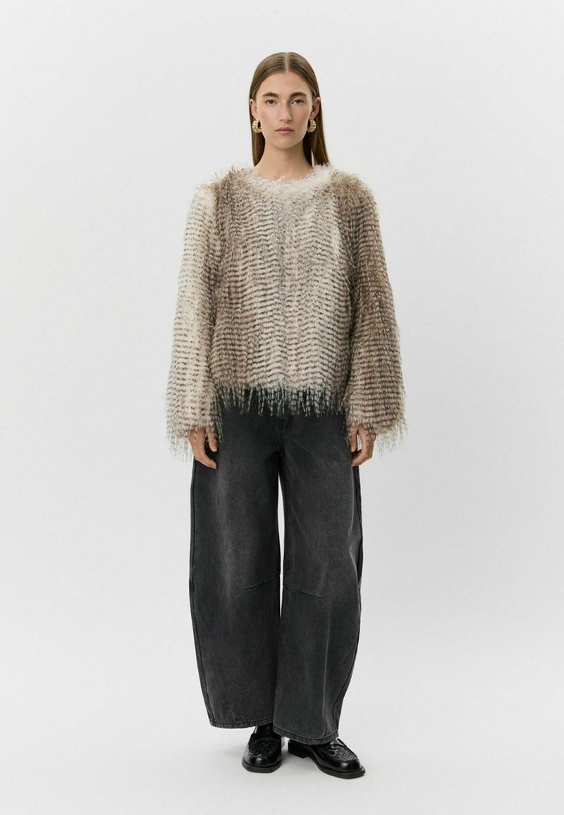 Teksturirani, svijetložuti pulover s resama na rubu, nošen preko širokih crnih traperica. Masivni pleteni dizajn s horizontalnim linijama.