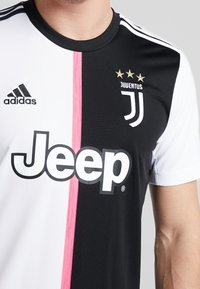 Camiseta de fútbol de la Juventus con un diseño dividido en blanco y negro, con una franja central rosa, los logos de adidas y Jeep, y tres estrellas doradas.