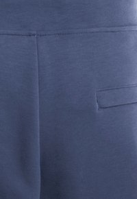 Materiał w kolorze granatowym o gładkiej fakturze. Posiada tylną kieszeń z detalami przeszycia. Projekt jest prosty, bez wzorów ani zdobień.