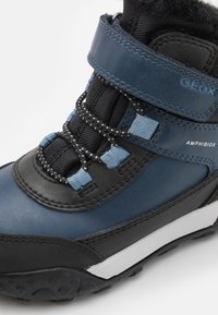 Modrá a černá turistická bota s reflexními tkaničkami, suchým zipem, značkou "GEOX" a "AMPHIBIOX", s robustní černou podrážkou a bílým mezipodešvem.