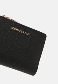 Black leather wallet with a textured surface, featuring a gold-tone logo and zipper hardware on the top edge.