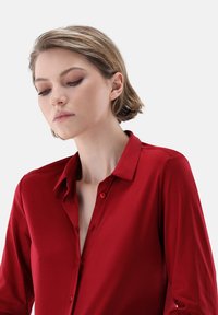 Camicia rossa con bottoni realizzata in un tessuto liscio, con colletto classico, maniche lunghe e una vestibilità leggermente rilassata.