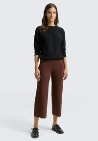 Zwart gebreid sweater met lange mouwen, gecombineerd met hooglopende, wijde bruine broek met verticale naden en een zachte textuur. Zwarte veterschoenen.
