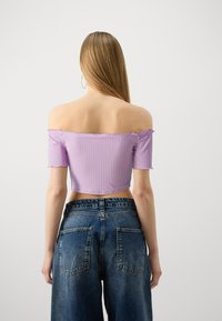 Top corto de canalé en color púrpura, con los hombros al descubierto y bordes deshilachados, combinado con unos jeans de mezclilla azules de tiro alto que presentan un diseño de bolsillo clásico.