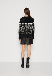 Maglione nero peloso con motivi geometrici bianchi, abbinato a una gonna di pelle nera. La modella indossa stivali neri fino al ginocchio.