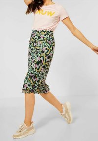 Floral pencil skirt in green, yellow, pink, and black, made from lightweight fabric. Paired with a pink graphic t-shirt and beige sneakers.