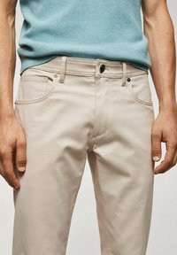 Lichtbeige katoenen broek met een rechte pasvorm, voorzien van een sluiting met een knoop aan de voorkant, twee zijzakken en subtiele stikdetails.