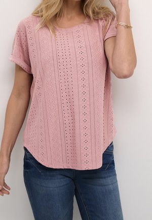 Lichtroze top met korte mouwen met oogjespatroon, ronde halslijn en gebogen zoom. Gecombineerd met donkerblauwe spijkerbroek, gepresenteerd tegen een neutrale achtergrond.