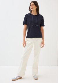Navy short-sleeve hoodie with a drawstring, paired with cream-colored wide-leg pants. Sneakers are light gray with brown accents.