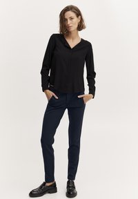 Čierna blúzka s dlhým rukávom a výstrihom do V, spárovaná s navy slim-fit nohavicami a čiernymi mokasínami. Tkanina vyzerá hladko a priedušne.