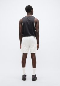 Μαύρο αμάνικο τοπ, λευκά σορτς, συνδυασμένα με μαύρα αθλητικά παπούτσια. Τα σορτς έχουν κορδόνι στη μέση, λεία υφή και ετικέτα στο πίσω μέρος.