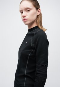 Must pikka varrukatega särk kaunist tekstuuriga pinnaga, kõrge kaelusega ja kontrastsete õmblustega. Rinnal on väike logo.