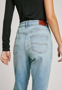 Heldere blauwe denim jeans met een hoge taille, voorzien van twee achterzakken en een bruine leren label op de tailleband. Gladde textuur, rechte pijpen.