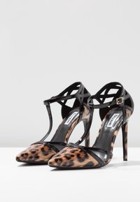 Décolleté in vernice nera con tessuto leopardato. Presenta un design a T-strap e punta affusolata, impostato su un sottile tacco a stiletto.