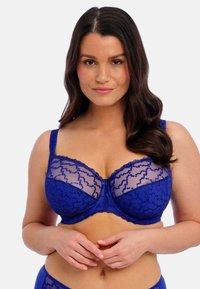 Soutien-gorge en dentelle bleue avec un superposé transparent, des motifs floraux, des bretelles réglables et un design en trois parties pour un soutien optimal. Texturé et délicat.