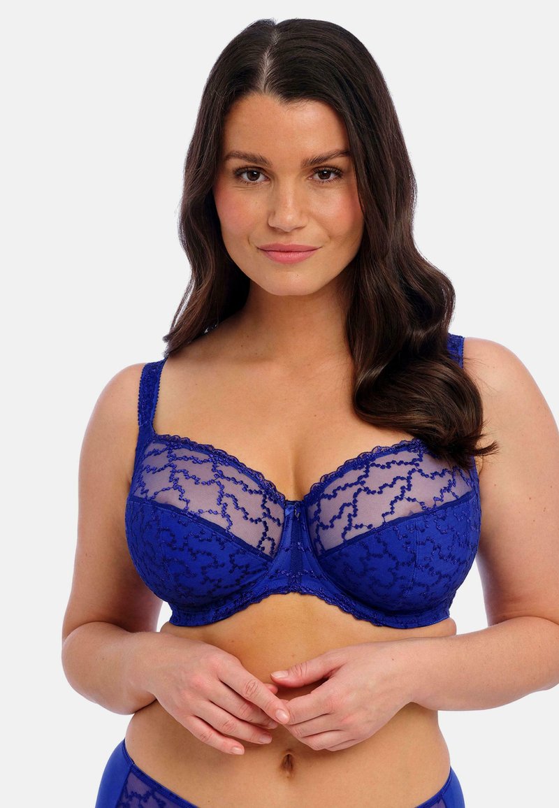 Soutien-gorge en dentelle bleue avec un superposé transparent, des motifs floraux, des bretelles réglables et un design en trois parties pour un soutien optimal. Texturé et délicat.