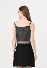 Svart mesh crop-top med hvite prikker, med tykke stropper med logo-detaler. Baksiden er litt gjennomsiktig, noe som skaper en lagdelt effekt.