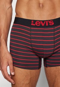 Svart och rödrandig boxerbriefs med ett mjukt midjeband som visar "Levi's" i rött. Tyget är slätt med en åtsittande design.