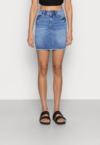 Jupe en denim mini de couleur bleu clair avec une coupe droite, un ourlet effiloché, un design à cinq poches et des passants de ceinture, associée à des sandales noires à larges brides.