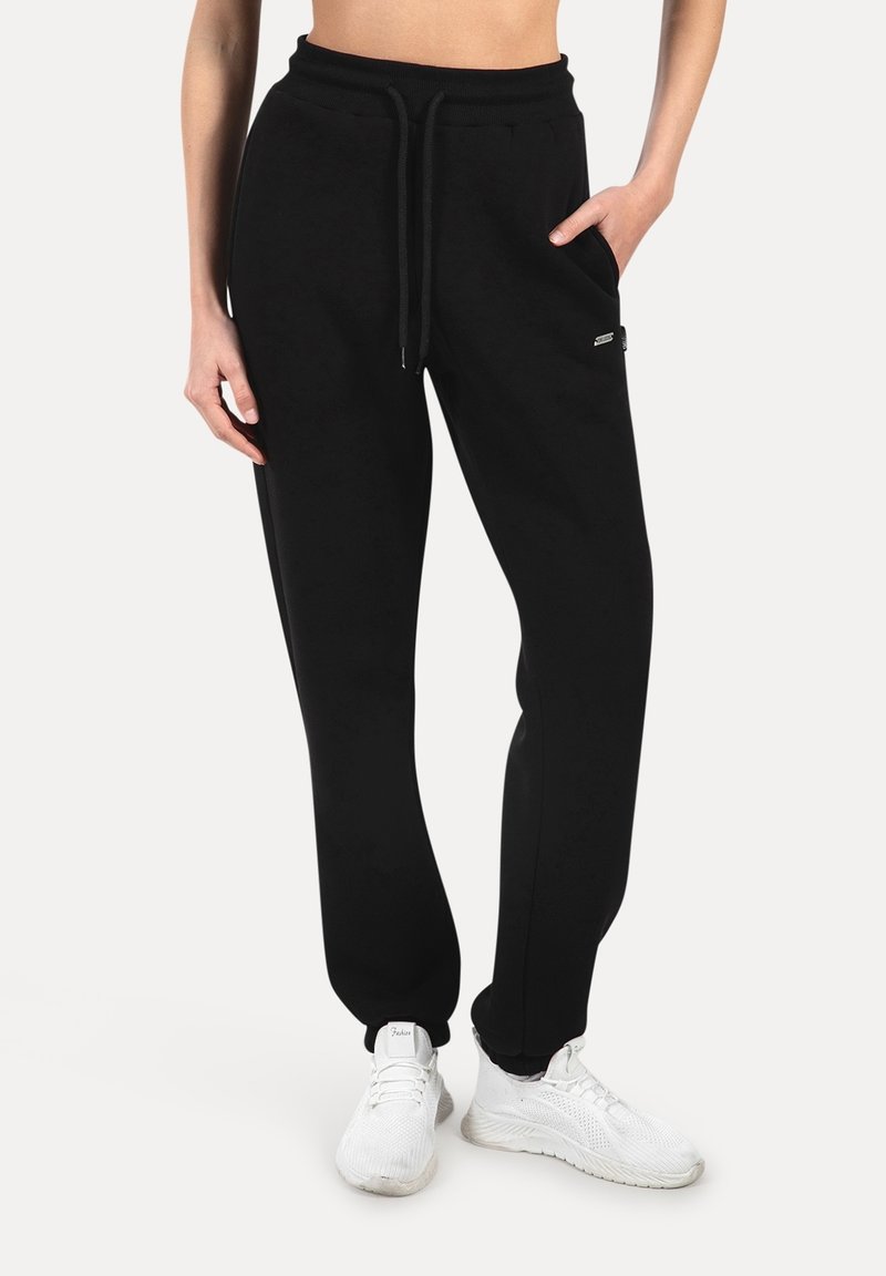 Pantalon de jogging noir en tissu doux, muni d'une ceinture élastique, d'un cordon de serrage et de poches latérales. Conçu pour une coupe décontractée.