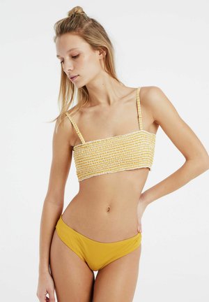 Geel en wit gestreepte, textuur gecreëerde crop top met dunne bandjes, gecombineerd met effen mosterdkleurige low-rise bikini onderkant. Glad materiaal, figuuraccentuerend ontwerp.